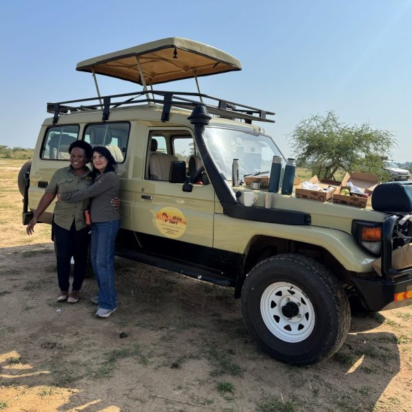 Two women smiling and posing in front of a safari car 