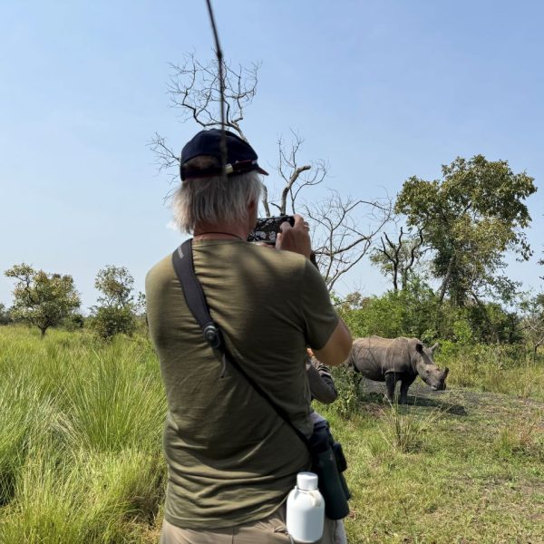 A man on a rhino trek taking a photo of a rhino at a distance 