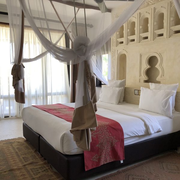 A hotel bed with white linen bed sheets and a red bed runner 