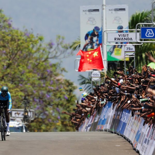 A cyclist riding along a paved road as supporters cheer him on 