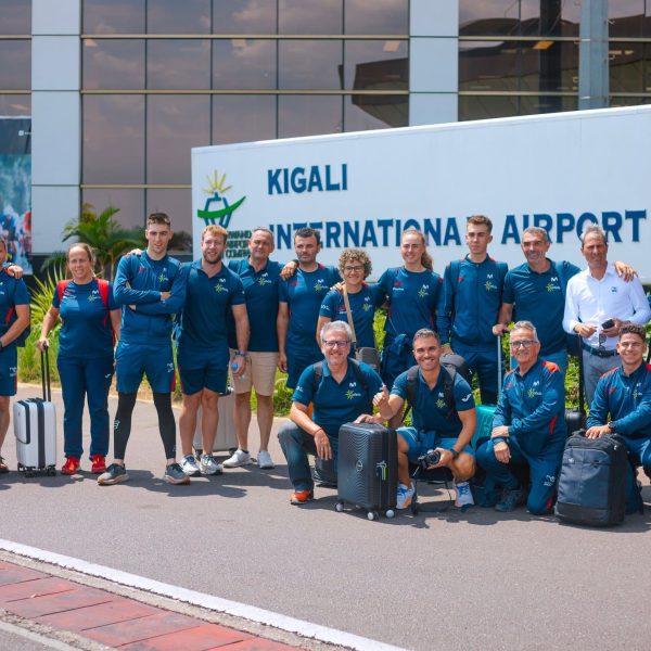 A team of humans standing in front of a Kigali International Airport sign post
